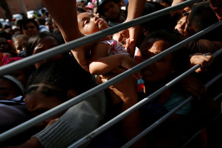 A baby is taken out from a crowd while her mother queues on the street with others as they try to buy diapers outside a pharmacy in Caracas, Venezuela March 18, 2017. REUTERS/Carlos Garcia Rawlins