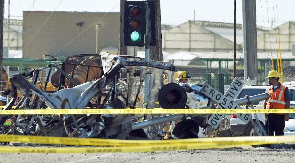 FILE - In this Feb. 24, 2015 file photo, a worker stands next to a railroad crossing sign and the wreckage of a truck that was struck by a Metrolink passenger train, causing it to derail in Oxnard, Calif. Federal investigators have determined that the crash that killed a Metrolink commuter train engineer was probably due to acute fatigue and lack of familiarity with the area by the driver of a utility truck that turned onto the tracks according to the National Transportation Safety Board's final report released Monday, Dec. 19, 2016. (AP Photo/Mark J. Terrill, File)