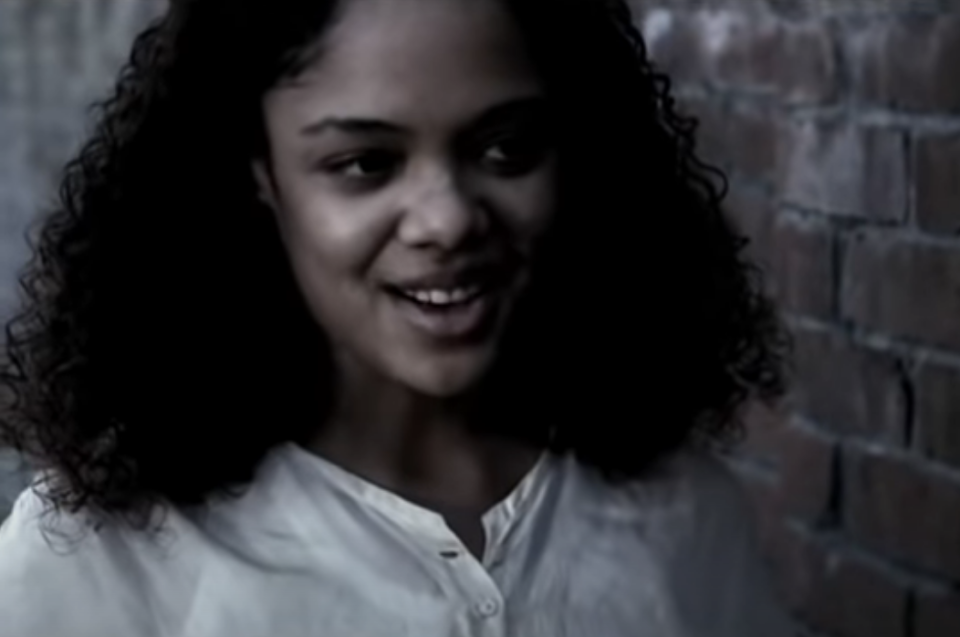 She's got curly hair wearing a casual shirt, standing near a brick wall