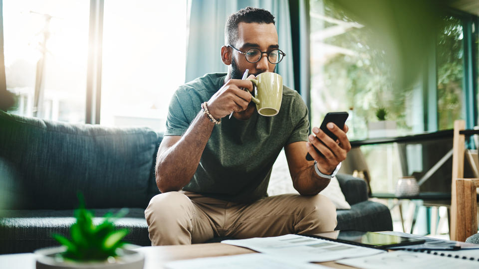 Shot of a young man using a smartphone while going over his finances at home.