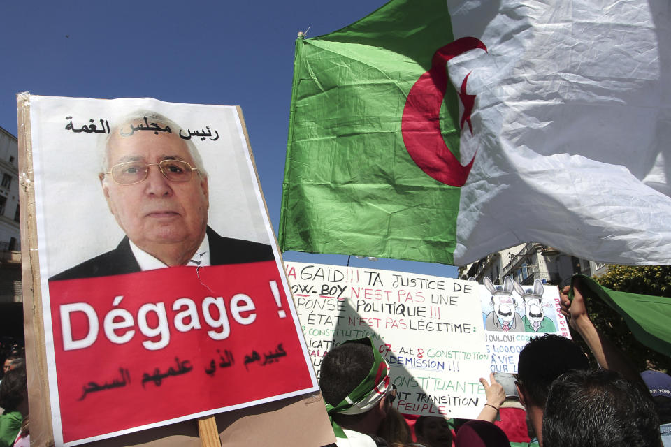 A demonstrator holds a placard showing Abdelkader Bensalah and reading "Get out" during a protest in Algiers, Friday, April 26, 2019. Algerians are massing for a 10th week of protests against their country's ruling class, calling for the ex-president's brother to be put on trial. (AP Photo/Fateh Guidoum)