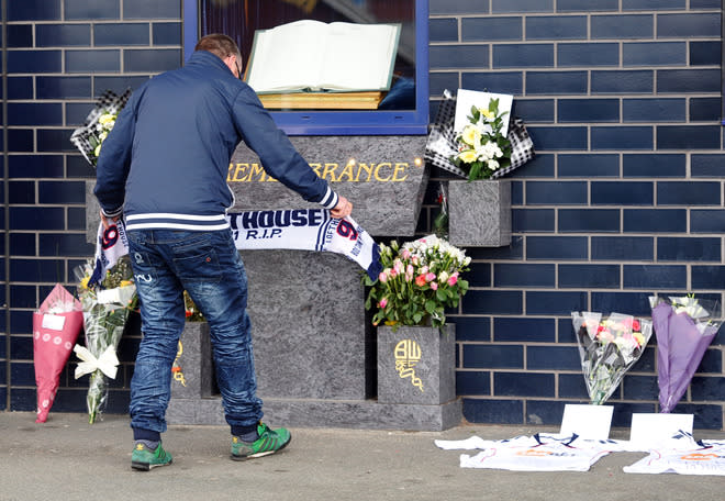 A man lays a scarf alongside football shirts and flowers left outside the Reebok Stadium in Bolton, north-west England on March 18, 2012 the morning after Bolton Wanderers' English midfielder Fabrice Muamba collapsed during their FA cup football match against Tottenham Hotspur in London. The 23-year-old Kinshasa-born player was rushed to hospital after harrowing scenes towards the end of the first half at White Hart Lane on Saturday, when the midfielder slumped to the turf with no player near him. TOPSHOTS AFP PHOTO / PAUL ELLIS