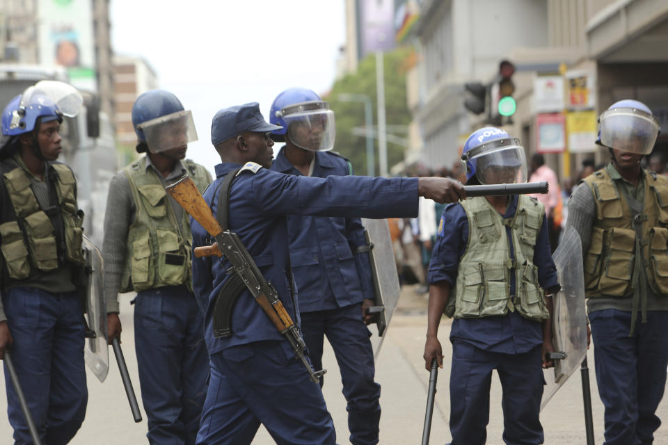 Police officers stand by as opposition party supporters gathered to hear a speech by the country's top opposition leader in Harare, Wednesday, Nov, 20, 2019. Zimbabwean police with riot gear fired tear gas and struck people who had gathered at the opposition party headquarters to hear a speech by the main opposition leader Nelson Chamisa who still disputes his narrow loss to Zimbabwean President Emmerson Mnangagwa. (AP Photo/Tsvangirayi Mukwazhi)