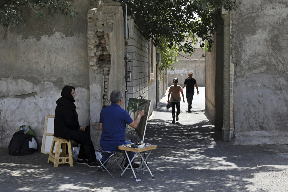 Painter Hassan Naderali paints an old building as his assistant Minoo Amini looks on in the historic neighborhood of Oudlajan, in Tehran, Iran, Monday, June 20, 2022. The overcrowded metropolis may be dusty and in need of beautification, but the old alleyways are nonetheless drawing throngs of artists out of their studios and into the streets. The practice thrived during the pandemic, as artists found solace and inspiration under the open sky when galleries and museums shuttered. (AP Photo/Vahid Salemi)