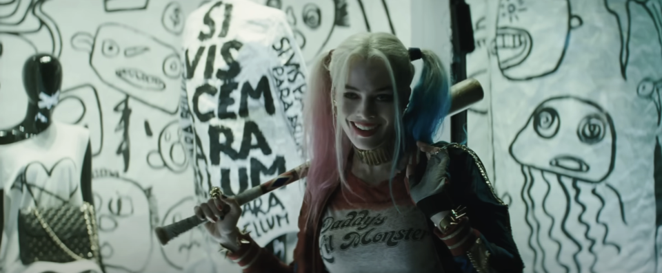 Harley Quinn stands with a bat over her shoulder in front of graffiti walls