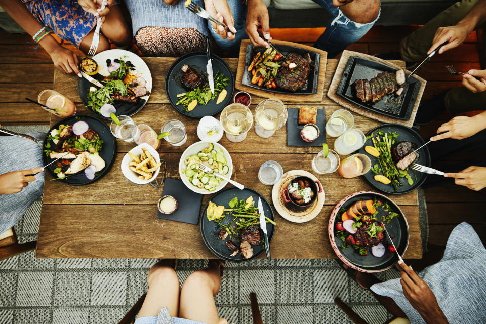 Group of people dining at a table with various dishes and drinks, sharing a meal together