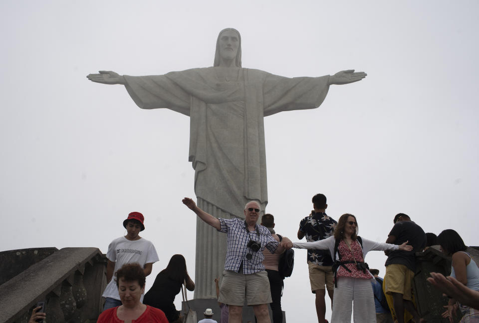 Tourists pose for photos in front of the Christ the Redeemer statue during a foggy day in Rio de Janeiro, Brazil, Tuesday, March 17, 2020. The company that administers transport and installations at Rio's Sugarloaf Mountain, another postcard destination that sees 1.5 million visitors annually, said it is closing shop on Tuesday for 15 days as a measure to prevent the spread of the new coronavirus. (AP Photo/Silvia Izquierdo)