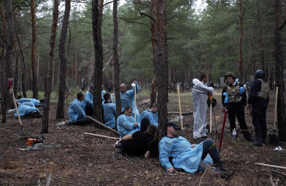 Emergency workers have a rest during the exhumation of bodies in the recently retaken area of Izium, Ukraine, Friday, Sept. 16, 2022. Ukrainian authorities discovered a mass burial site near the recaptured city of Izium that contained hundreds of graves. It was not clear who was buried in many of the plots or how all of them died, though witnesses and a Ukrainian investigator said some were shot and others were killed by artillery fire, mines or airstrikes. (AP Photo/Evgeniy Maloletka)