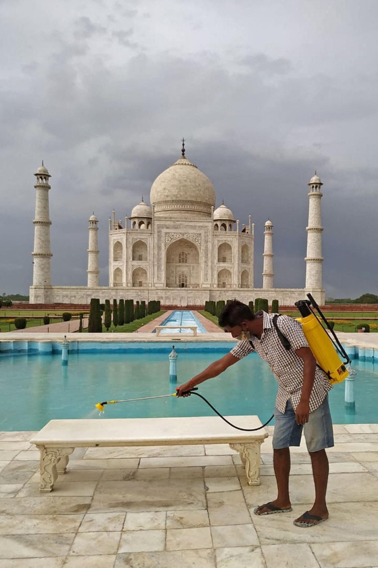 A sanitation worker sprays disinfectant on the marble bench at the premises of Taj Mahal mausoleum on the eve of its reopening to public after two months due to the lockdown (AFP via Getty Images)