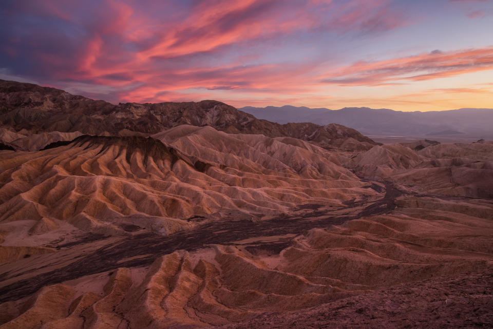 Sunset over rugged desert terrain with layered rock formations