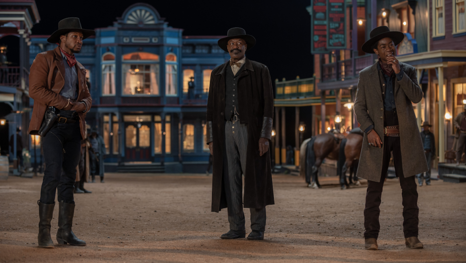 Jonathan Majors, Delroy Lindo, and R.J. Cyler wear Old West garb in a nighttime small town setting.