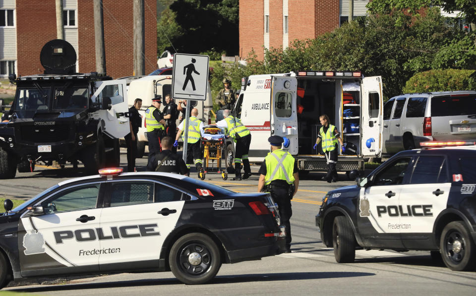 Police officers and paramedics survey the area of a shooting in Fredericton, New Brunswick, Canada on Friday, Aug. 10, 2018. Fredericton police say two officers were among four people who died in a shooting Friday in a residential area on the city's north side. One person was in custody, they said, and there was no further threat to the public. (Keith Minchin/The Canadian Press via AP)