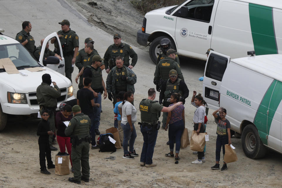 FILE - In this Dec. 10, 2018, file photo, a girl waves to a young man watching from Mexican territory who said he was her cousin, as a group of Honduran asylum seekers is taken into custody by U.S. Border Patrol agents after the group crossed the U.S. border wall into San Diego, seen from Tijuana, Mexico. San Diego County has approved a plan to provide attorneys to immigrants facing deportation proceedings. The Board of Supervisors on Tuesday, May 4, 2021 approved a $5 million, one-year pilot program. It would provide lawyers for free to those detained at Otay Mesa Detention Center, the local federal immigration detention facility. San Diego will be the first southern border county in the U.S. to provide such legal representation. (AP Photo/Rebecca Blackwell, File)