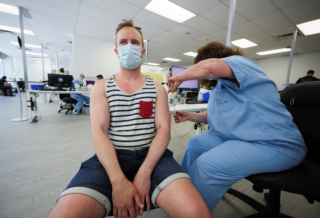 A man in a mask wearing a striped, sleeveless shirt receives a monkeypox vaccination.