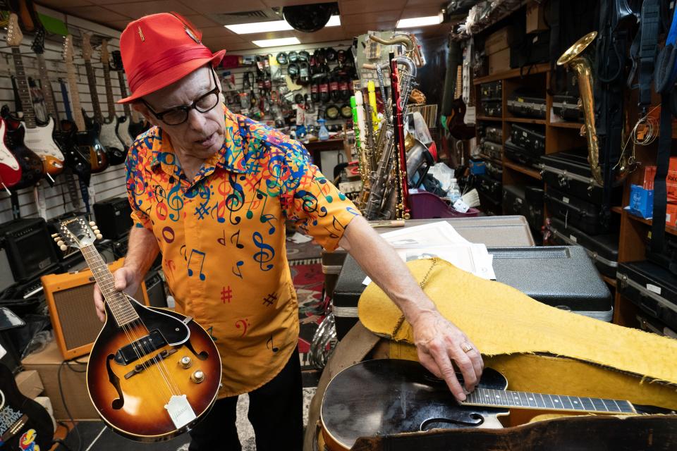 While holding a Gibson mandolin, Jimmy Hayes, owner of Hayes House of Music, points out the details and advantages to a Shutt mandolin including a slightly longer fret board to accommodate more notes than the Gibson.