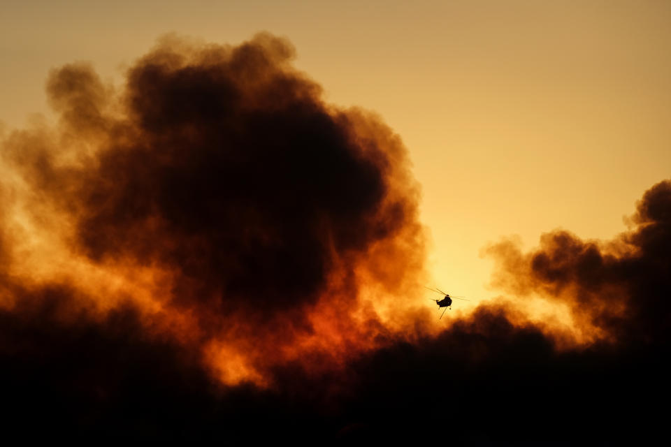 A helicopter flies over smoke rising from a wildfire during sunset Wednesday, Oct. 13, 2021, in Goleta, Calif. (AP Photo/Ringo H.W. Chiu)