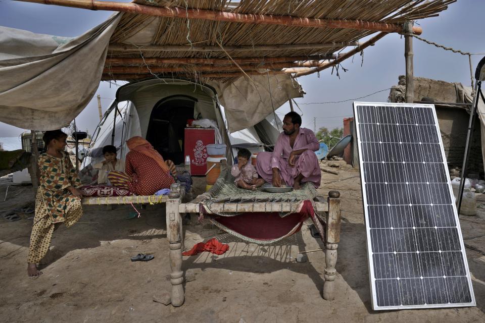 A flood victim, Muhammad Ibrahim, and his family eat rice next to a solar panel used for electricity in Ismail Khan Khoso village in Sohbatpur, a district of Pakistan's Baluchistan province, Thursday, May 18, 2023. In rural areas of Baluchistan, only those who saved their solar panels from the flooding have access to electricity to keep cool in the summer heat. (AP Photo/Anjum Naveed)