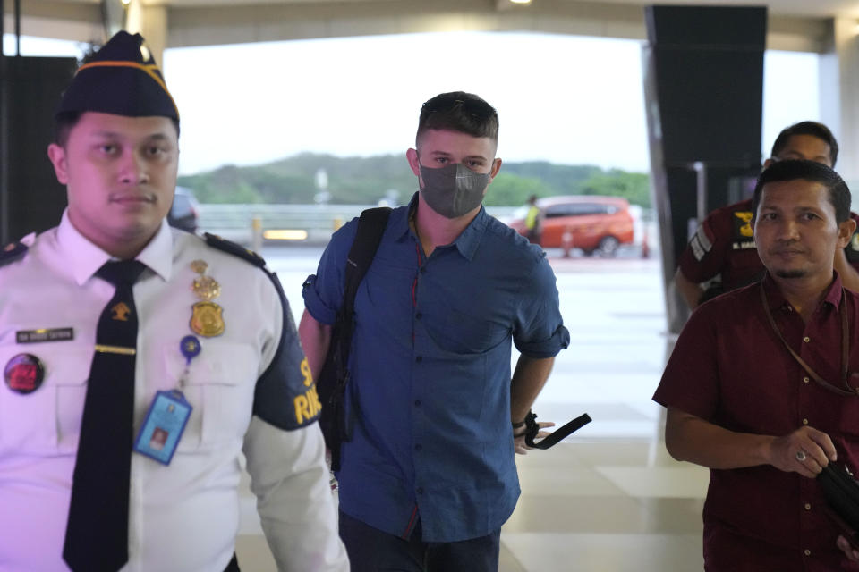 Australian national Bodhi Mani Risby-Jones from Queensland, center, walks with his lawyer Idris Marbawi, right, and an immigration officer upon arrival at Soekarno-Hatta International Airport in Tangerang, Indonesia, Saturday, June 10, 2023. Indonesia’s authorities are deporting an Australian surfer who apologized for attacking several people while drunk and naked in the deeply conservative province of Aceh. Bodhi Mani Risby-Jones was detained in late April on Simeulue Island, a surf resort, after police accused him of going on a drunken rampage that left a fisherman with serious injuries. (AP Photo/Dita Alangkara)