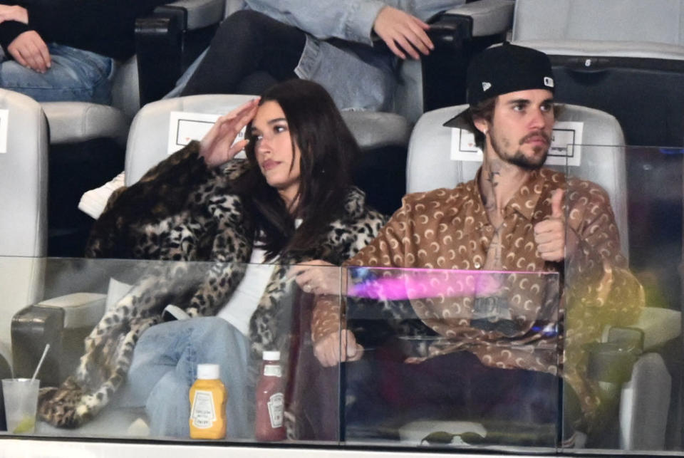 the Biebers at the Super Bowl, Hailey in a leopard print coat and Justin wearing a patterned shirt and cap