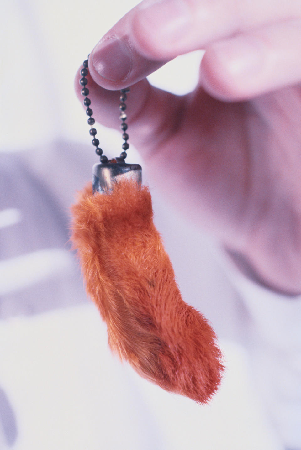 A hand holding a keychain with a small, fuzzy orange object attached. The context of the image is unclear