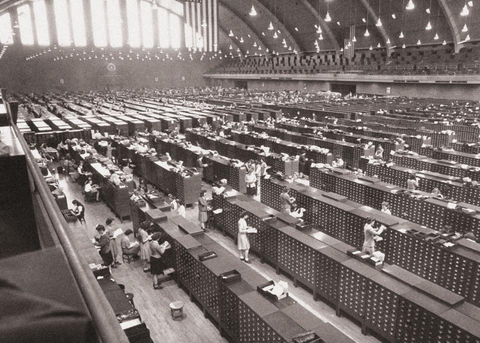 People and many stacks of small drawers in a large, cavernous room