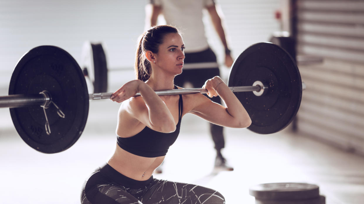  Woman performing loaded front squat with a barbell. 