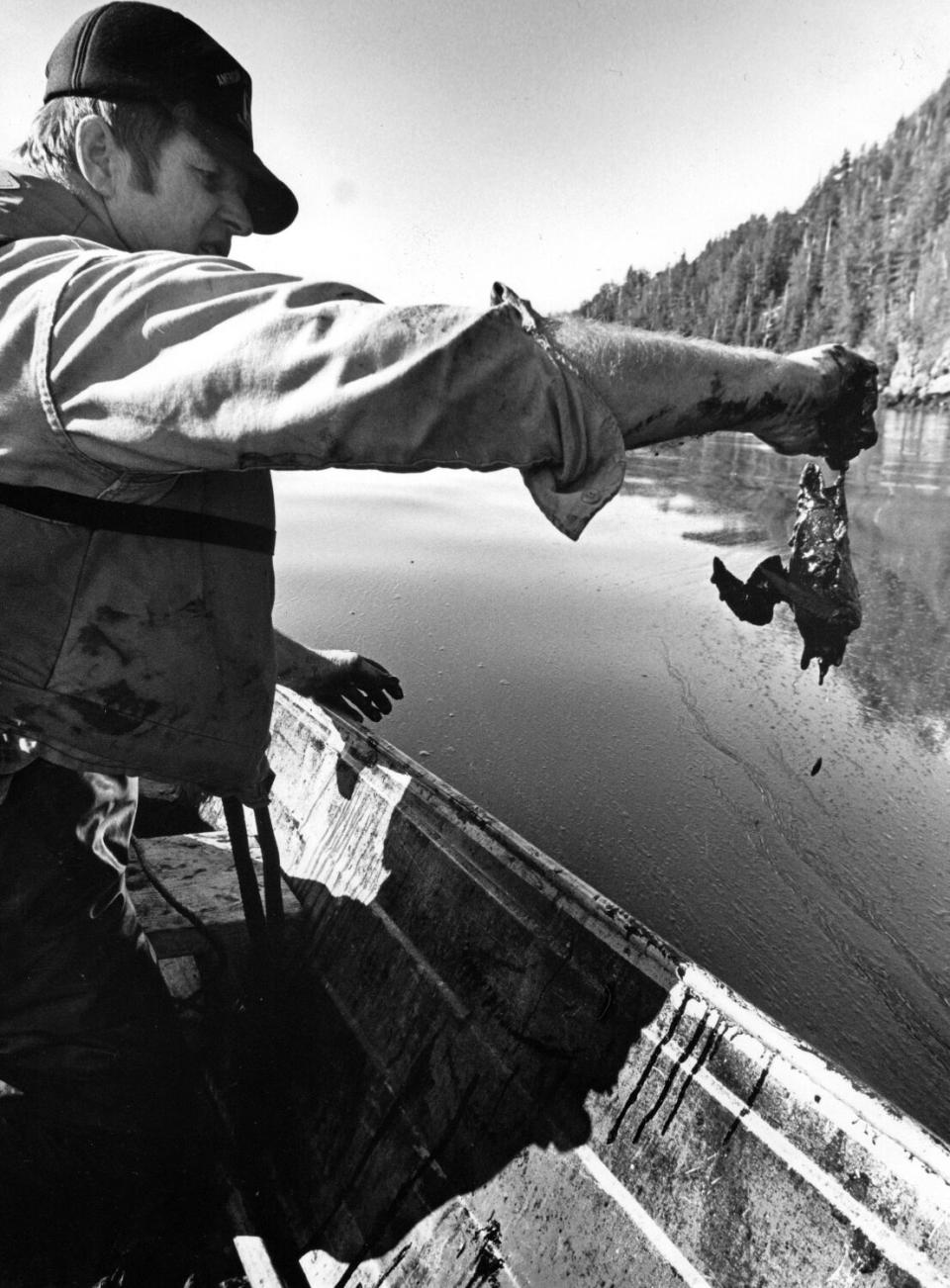 A man holds a dead, oil-covered bird.