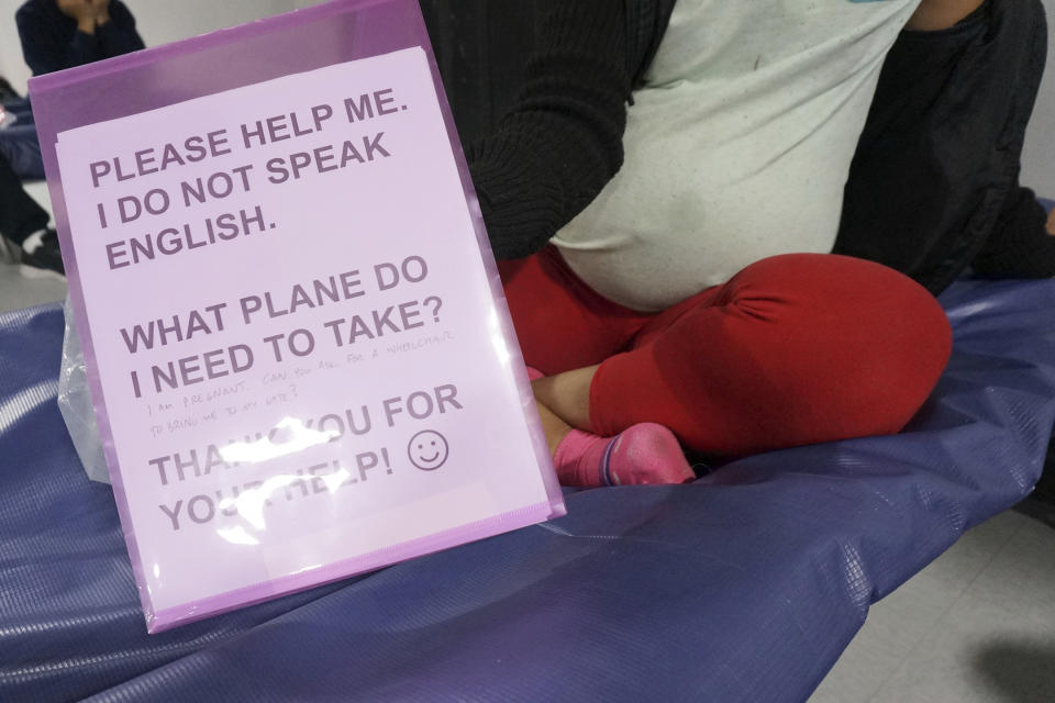 Gloria, a 22-year-old migrant from Honduras 8 months pregnant with her first child, sits on a cot in the Humanitarian Respite Center run by Catholic Charities across the bus station in McAllen, Texas, on Dec. 15, 2022. She holds a sign on which a visiting Catholic priest handwrote "I'm pregnant. Can you ask for a wheelchair to bring me to my gate?" after she said she was worried she didn't know how to navigate the connecting flights that will take her to an acquaintance in Florida. (AP Photo/Giovanna Dell'Orto)