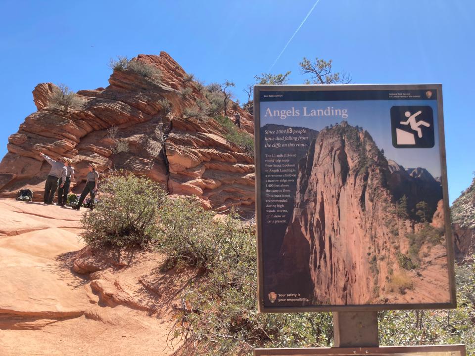 A sign just in front of the Angels Landing trail warns hikers of the dangers ahead. In the background, Zion National Park rangers enforce a new permit system designed to keep the trail from getting too crowded on April 1, 2022, the first day permits were required.