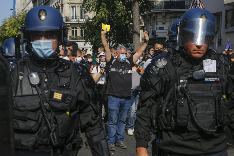 A yellow vest protester wearing protective face masks as precaution against the conoravirus holds up a yellow card during a march in Paris, Saturday, Sept. 12, 2020. Activists relaunched France's yellow vest movement Saturday after the disruptive demonstrations against Emmanuel Macron's presidency and perceived elitism tapered off during the coronavirus pandemic.(AP Photo/Michel Euler)