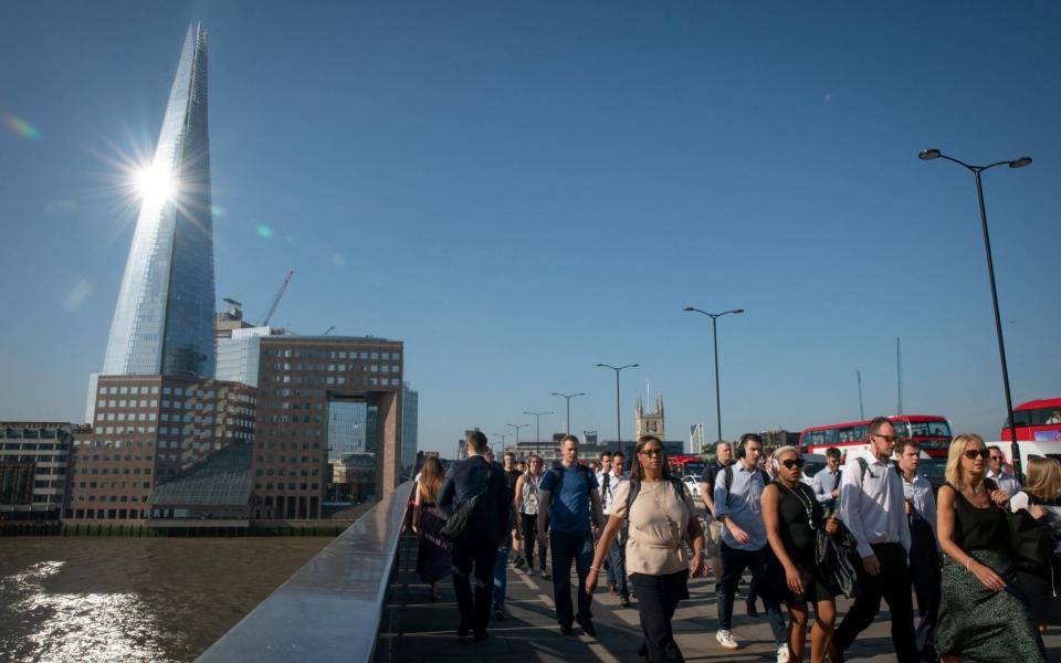 Commuters cross London Bridge as the sun beams off The Shard - SWNS