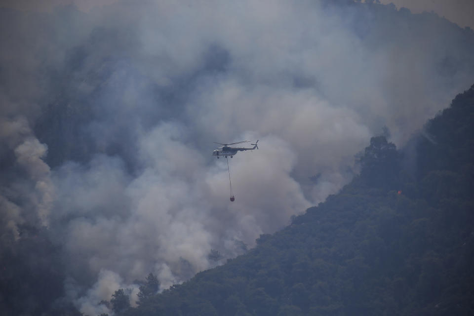 A firefighting helicopter flies over a wildfire that burns the forest in Turgut village, near tourist resort of Marmaris, Mugla, Turkey, Wednesday, Aug. 4, 2021. As Turkish fire crews pressed ahead Tuesday with their weeklong battle against blazes tearing through forests and villages on the country's southern coast, President Recep Tayyip Erdogan's government faced increased criticism over its apparent poor response and inadequate preparedness for large-scale wildfires.(AP Photo/Emre Tazegul)