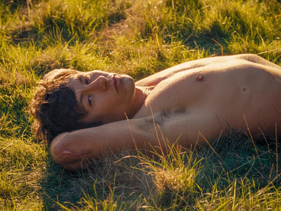 Oliver lies shirtless in the grass in a scene from "Saltburn"