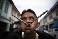 PHUKET, THAILAND - OCTOBER 04: A devotee of the Chinese shrine of Kathu Shrine, pierces his cheeks with power drills during a procession at the Vegetarian Festival on October 4, 2011 in Phuket, Thailand. Ritual Vegetarianism in Phuket Island traces it roots back to the early 1800's. The festival begins on the first evening of the ninth lunar month and lasts for nine days. Participants in the festival perform acts of body piercing as a means of shifting evil spirits from individuals onto themselves and bring the community good luck. (Photo by Athit Perawongmetha/Getty Images)