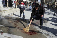 An Afghan man sweeps blood after Gunmen fired in Kabul, Afghanistan, Sunday, Jan. 17, 2021. Gunmen fired on a car in northern Kabul on Sunday, killing two women judges who worked for Afghanistan's high court and wounding the driver, a court official said. It was the latest attack in the Afghan capital during peace talks between Taliban and Afghan government officials in Qatar. (AP Photo/Rahmat Gul)