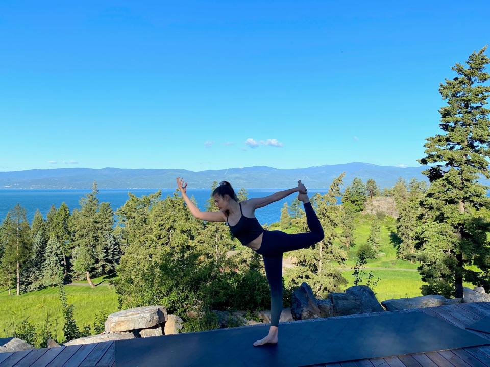 A woman doing a yoga pose in front of a scenic lookout point of mountains and trees.