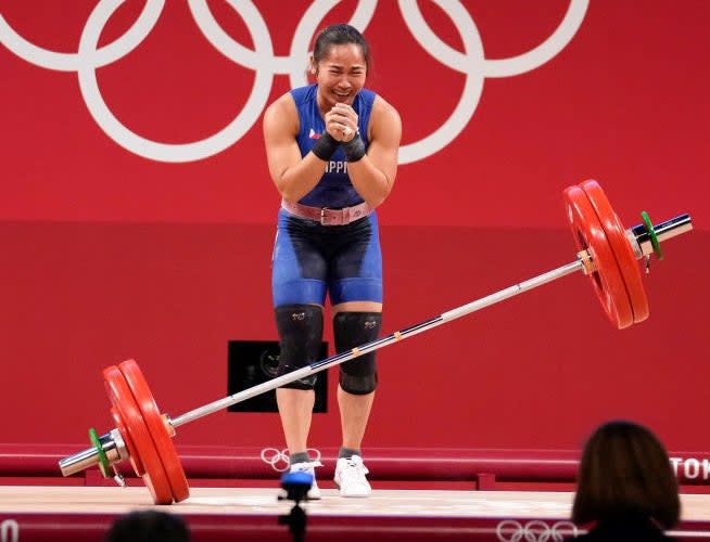 Hidilyn holding her hands together and smiling as the weight drops to the floor