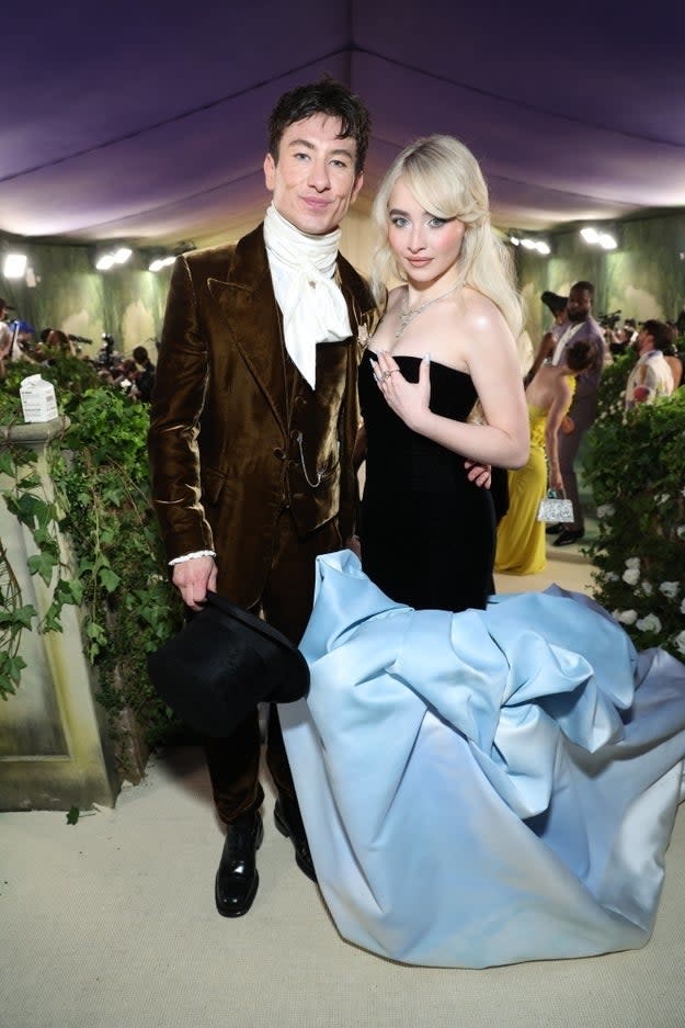 Barry Keoghan in a velvet suit and top hat, with Chloe Fineman in a black dress with a large blue train, at a formal event