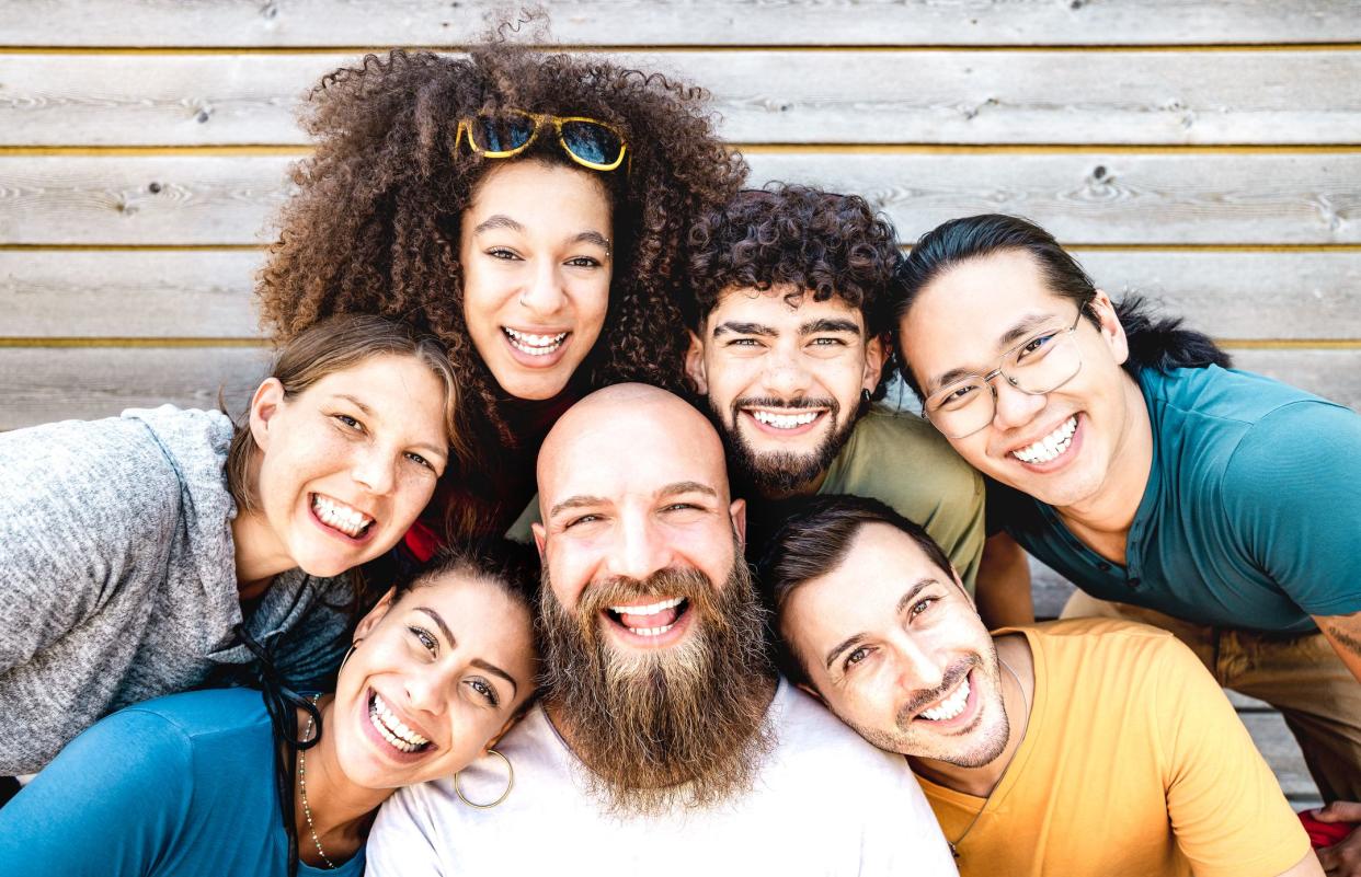 Multicultural guys and girls taking selfie outdoors on wooden background - Happy milenial life style concept with young multiethnic hipster people having fun day together - Warm bright filter