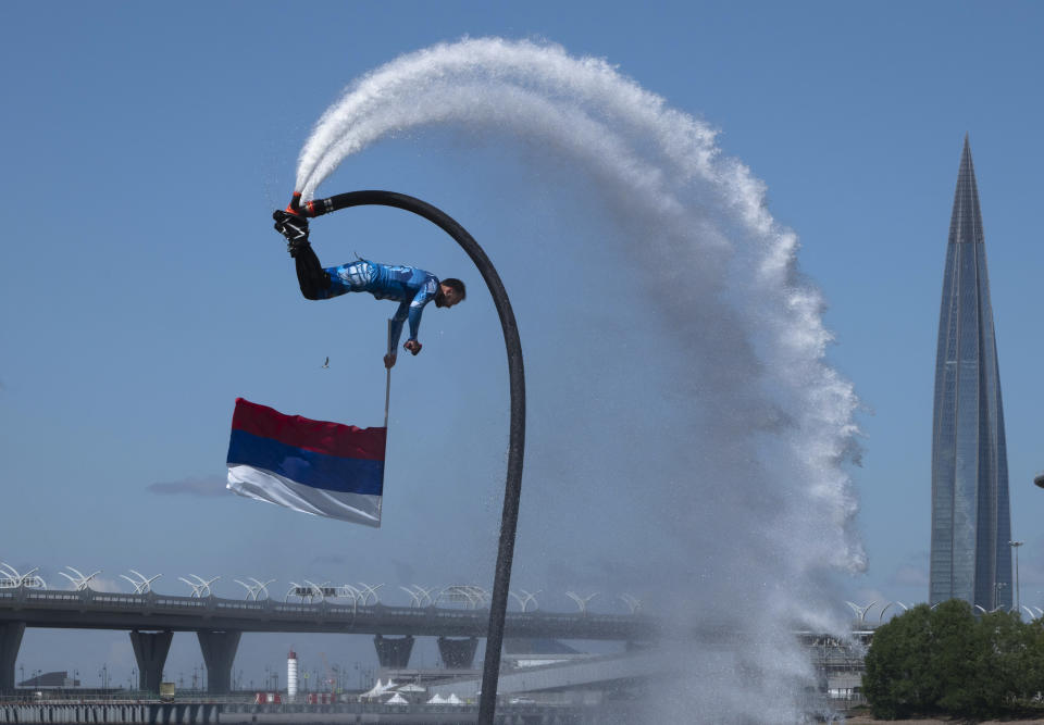 A members of the Russian hydroflight team performs holding the Russian national flag during the Day of Russia celebration in St.Petersburg, Russia, Friday, June 12, 2020, with business tower Lakhta Centre, the headquarters of Russian gas monopoly Gazprom in the background. (AP Photo/Dmitri Lovetsky)