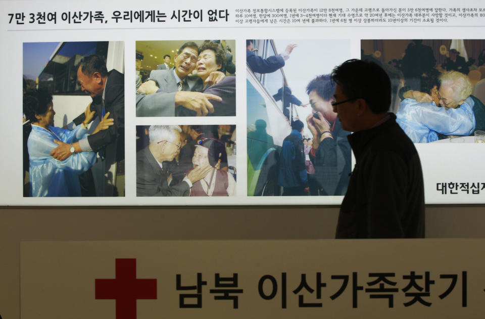 An employee of the Red Cross passes by the pictures showing some reunions of family members from North and South Korea, at the headquarters of the Korea Red Cross in Seoul, South Korea, Thursday, March 6, 2014. Seoul said that North Korea rejected Seoul's proposal to hold talks on reunions of families divided by the 1950-53 Korean War. South Korea wants to make such reunions, which were held last month for the first time in more than three years, become regular events, but analysts say Pyongyang worries that could take away a key piece of political leverage with the South. The Korean writing at bottom reads " Applications reception of separated families." (AP Photo/Ahn Young-joon).