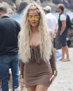 <p>Khloé wears her hair in long, beachy waves with a brown slinky mini with tie-front detail, mirrored sunglasses and chunky gold bangles. </p>