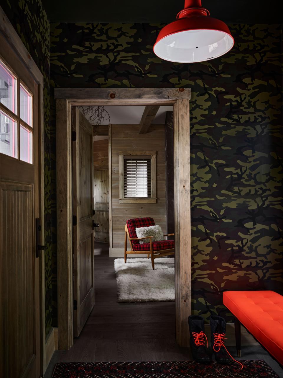 In the compact foyer, an upholstered bench—once again in hunting-blaze orange—sits in front of custom camouflage wallpaper. The space offers a peek through to the living room beyond.