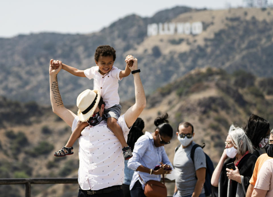 Some visitors wear face masks outdoors while taking pictures of the Hollywood sign at the Griffith Observatory in Los Angeles, Monday, May 17, 2021. California is keeping its rules for wearing face masks in place until the state more broadly lifts its pandemic restrictions on June 15. (AP Photo/Damian Dovarganes)