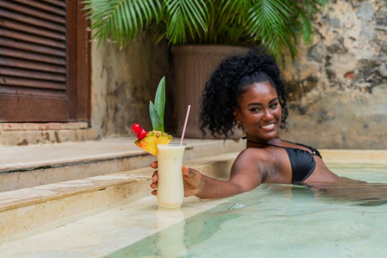 woman smiling with a mocktail while sitting in a pool