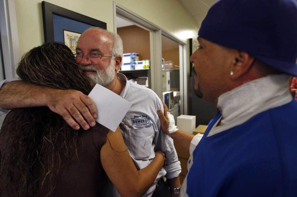 El padre Gregory Boyle, en el centro, abrazó a Nancy Delgadillo mientras David Minjarez vio la sede de Homeboy Industries en Los Ángeles, California, el 14 de septiembre de 2010. Minjarez tiene el cuello vendado después de que le quitaran un tatuaje en Homeboy Industries.