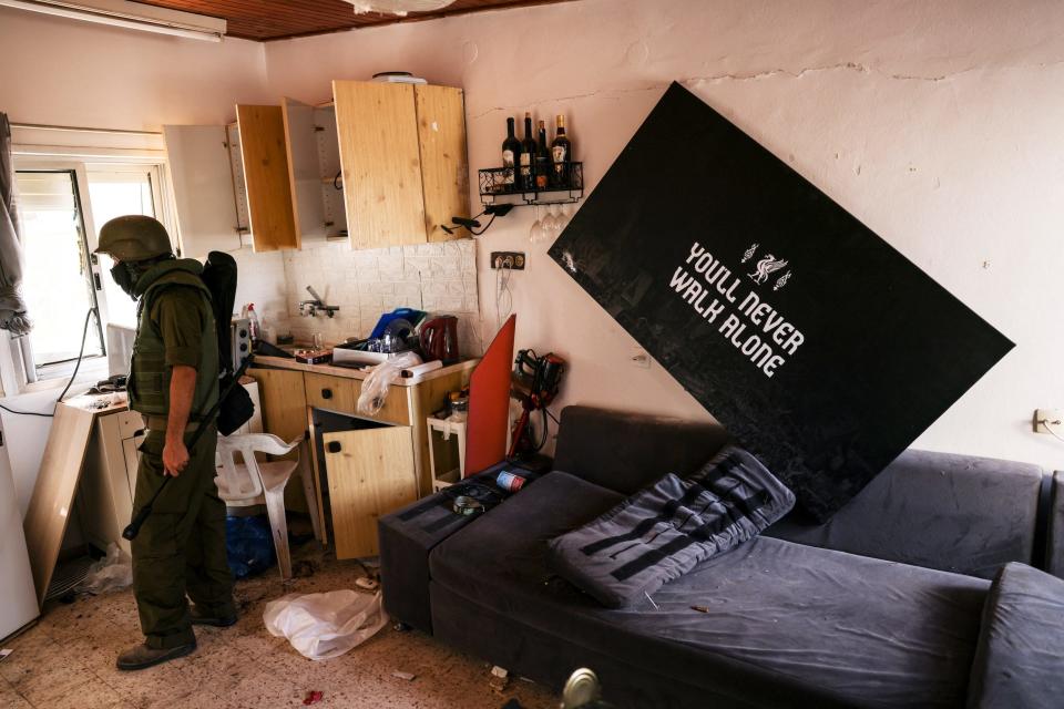 A photo of a soldier walking through an abandoned home with a crooked poster that reads "You'll never walk alone."