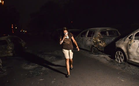 A woman walks in front of burnt cars at the village of Mati during a wildfire near Athens - Credit: AFP