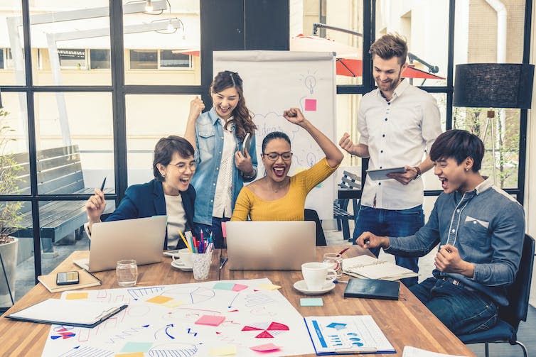 A group of people in an office celebrate and look happy.