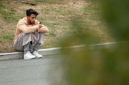 A man sits on the sidewalk after attending the burial ceremony of the victims of the mosque attacks, at the Memorial Park Cemetery in Christchurch, New Zealand March 21, 2019. REUTERS/Edgar Su